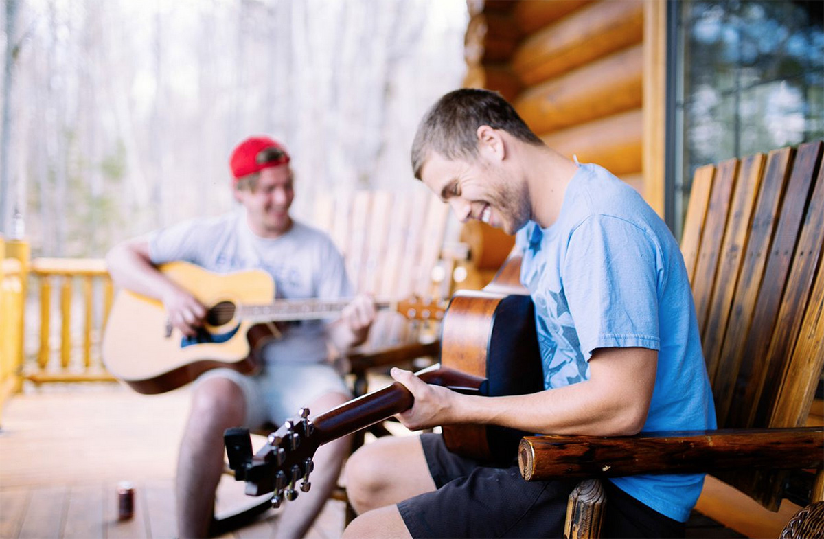 nathaniel wolkstein smiling playing acoustic guitar at a cabin